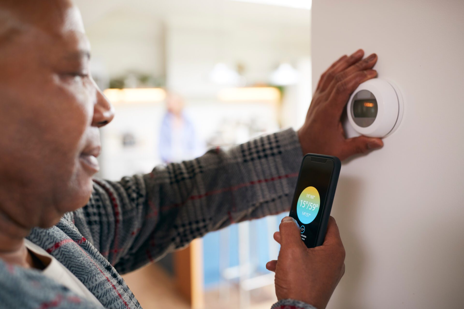 Mature Man Using App On Phone To Control Digital Central Heating Thermostat At Home